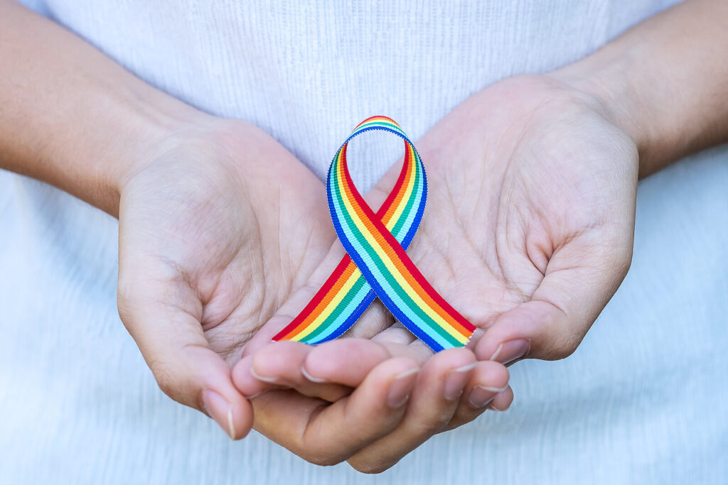 Hand Showing Lgbtq Rainbow Ribbon Against Sky Background(1)